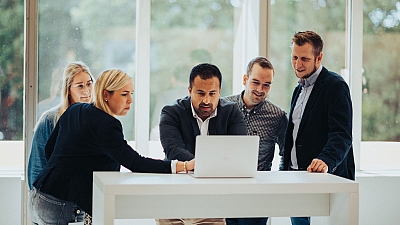 Besonders in Projekten ist Team-Arbeit Trumpf. Mehrere LBS NordWest Mitarbeiter stehen um einen Laptop.