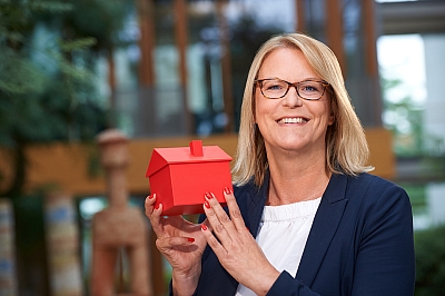 LBS-Kollegin-lächelt-mit-rotem-Haus-in-der-Hand-in-die-Kamera LBS Kollegin lächelt mit einem roten Haus in ihrer Hand in die Kamera im LBS Gebäude in Hannover