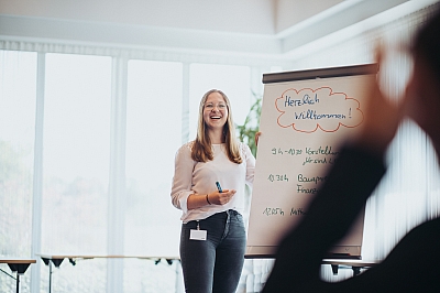 LBS-Kollegin-präsentiert-Inhalte-an-einem-Flipchart Junge LBS Kollegin lächelt beim Präsentieren von Inhalten an einem Flipchart