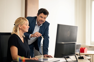 LBS-Gebietsleiter schaut LBS-Beraterin vor dem Computer über die Schulter und gibt Tipps.