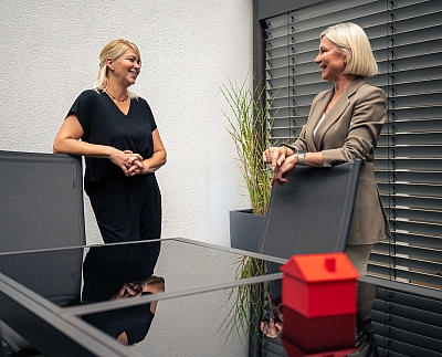 LBS-Beraterin-und-Gebietsleiterin-sind-auf-der-Terrasse-im-Gespräch-und-lächeln-sich-an LBS-Beraterin und Gebietsleiterin sind auf der Terrasse im Gespräch und lächeln sich an.